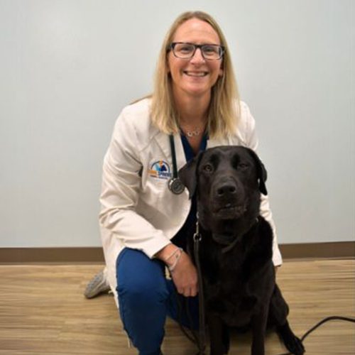 Dr Elizabeth Rawson with her black dog and smiling at the camera